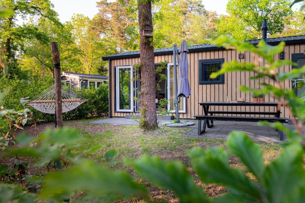 a log cabin with a hammock and a tree at Lodge Eik Nunspeet Veluwe in Nunspeet
