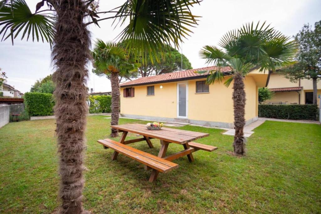 una mesa de picnic de madera en un patio con palmeras en Cozy and welcoming house with private garden en Lignano Sabbiadoro