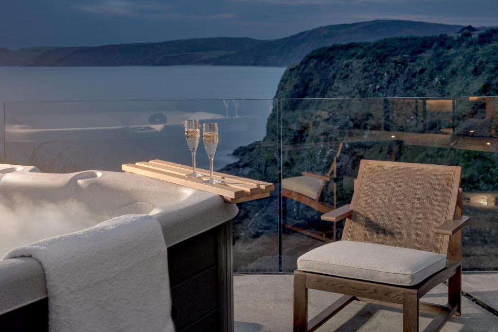 a bath tub with a chair and two glasses of wine at Edge House in Aberporth