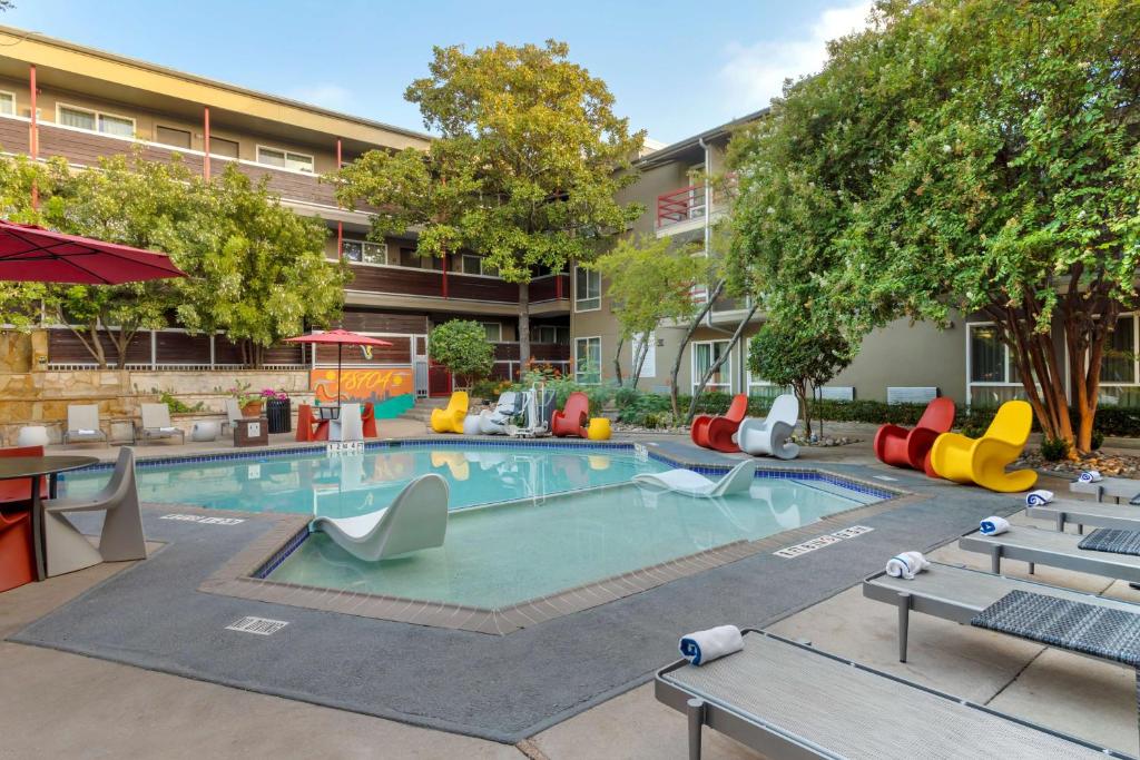 Aiden by Best Western Austin City Hotel في أوستن: حمام سباحة في الهواء الطلق مع كراسي وطاولات ملونة