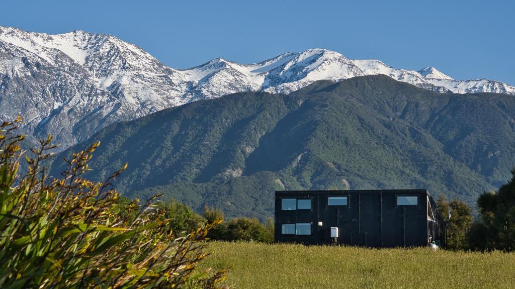 a house in a field with mountains in the background at Kanuka Terrace - The Little Black House in Hapuku