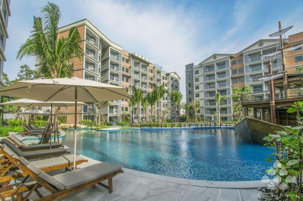 a swimming pool with an umbrella and chairs and buildings at Bright Apartment Close to Amazing Beach ! 39 Sqm in Nai Yang Beach
