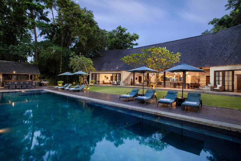 a swimming pool with chairs and umbrellas next to a house at Villa Tirtadari by Nakula in Canggu