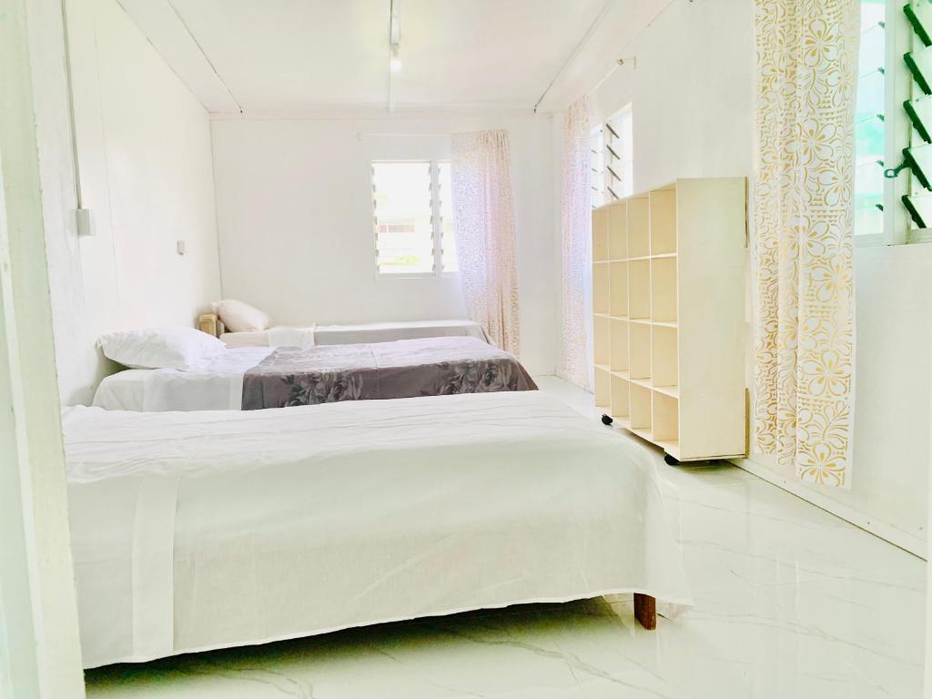 a white bedroom with two beds and a cabinet at Tonga Cottage - Triple Room with Shared Facilities in Folaha