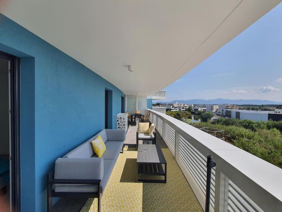 d'un balcon avec un canapé et des chaises sur un mur bleu. dans l'établissement Bleu Odysée Appartement 2 chambres, terrasse, équipé climatisation, place de parking à disposition, à Canet