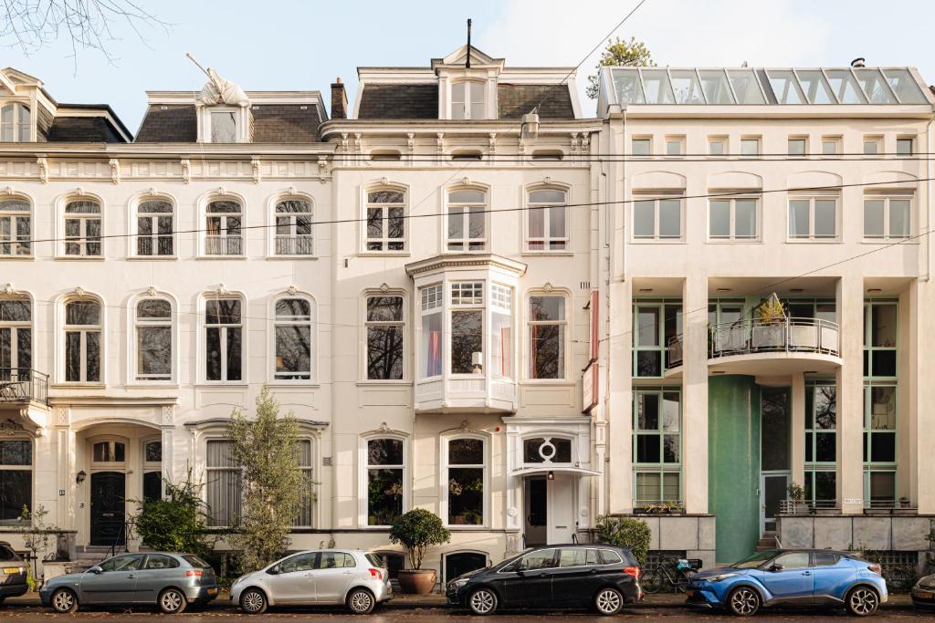 un grand bâtiment blanc avec des voitures garées devant lui dans l'établissement NEWLY OPENED - Parklane Hotel, à Amsterdam