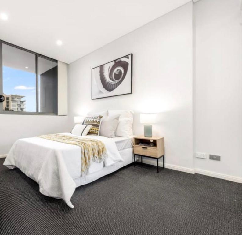 a white bedroom with a large bed and a table at Cozy stylish home in Rhodes in Sydney