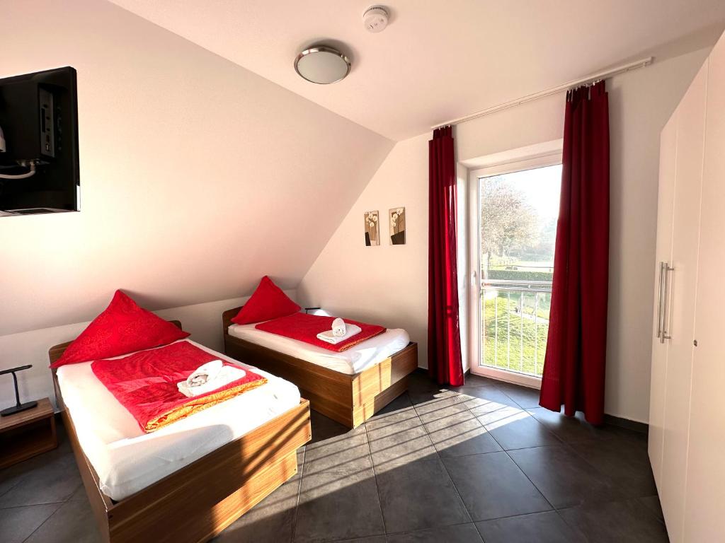a room with two beds and a window with red curtains at Gocher Berghof Ferienwohnungen Langanke in Goch
