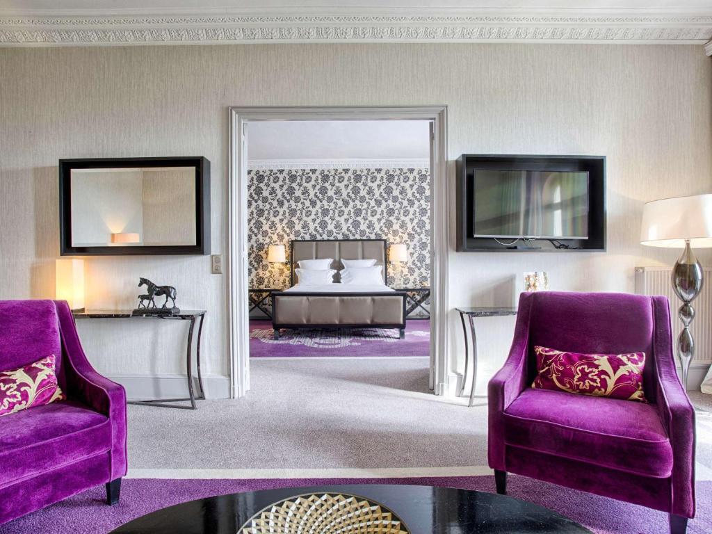 a bedroom with a bed and two purple chairs at Le Grand Hotel de Cabourg - MGallery Collection in Cabourg