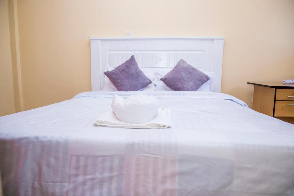 un cuenco blanco en una cama blanca con almohadas moradas en Elnara Suites, en Machakos