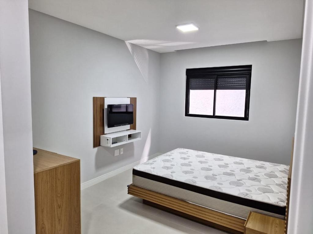 ein weißes Schlafzimmer mit einem Bett und einem Fernseher in der Unterkunft Areias de Bombas in Bombinhas