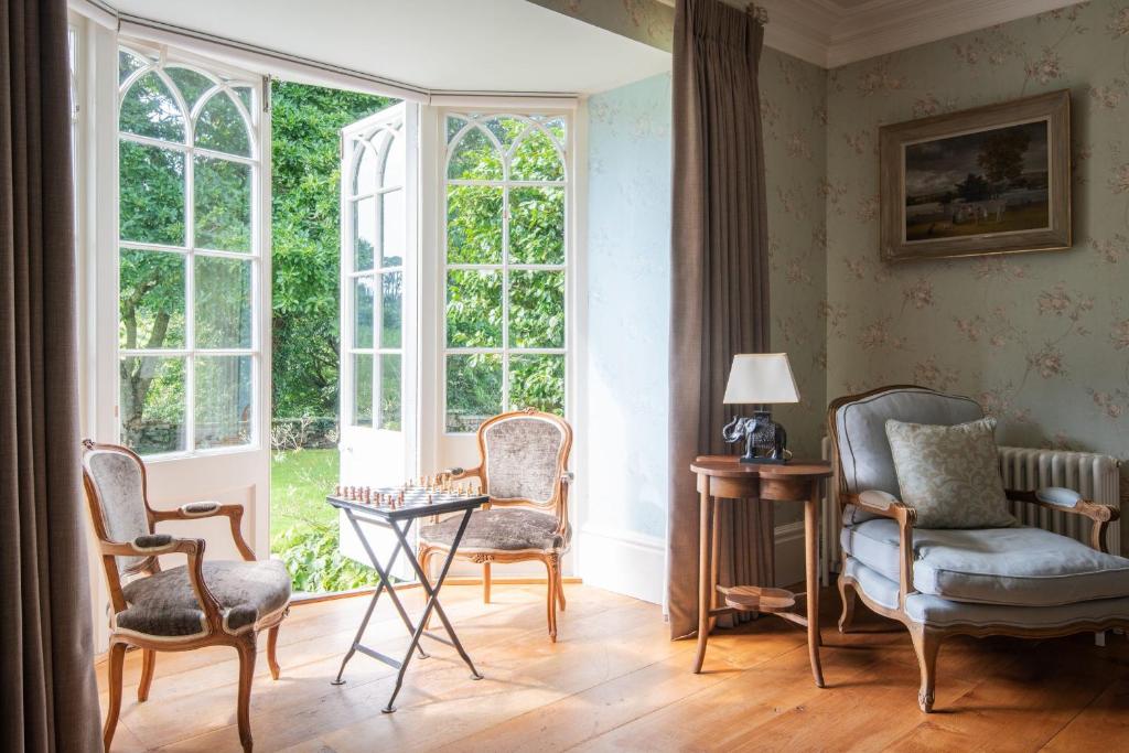 um quarto com duas cadeiras, uma mesa e janelas em Harlequin House em Holbeton