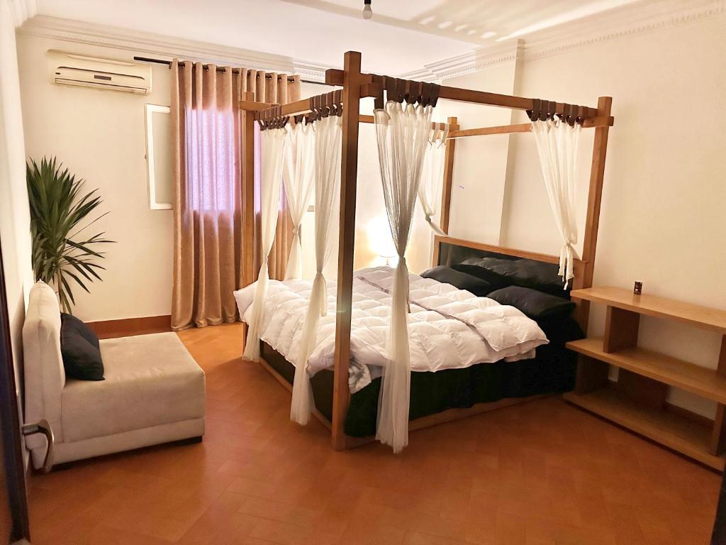 開羅的住宿－A lovely large master bedroom Maadi Degla，一间卧室配有一张带窗帘和椅子的天蓬床