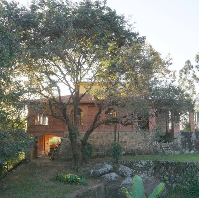 una casa de ladrillo con un árbol delante de ella en Casa rústica cercada de natureza em Atibaia, en Atibaia