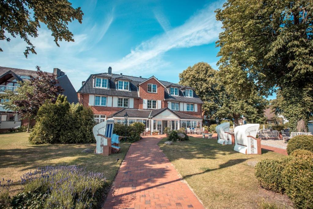 uma casa grande com cadeiras brancas no quintal em Strandhotel Strande em Strande