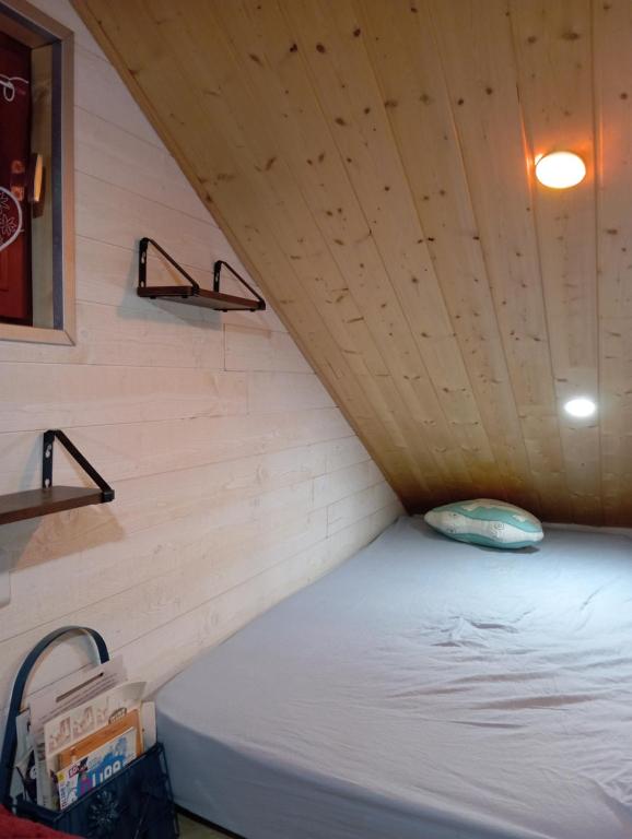 Cama en habitación pequeña con techo de madera en La p'tite maison bois du hérisson en Ménétrux-en-Joux