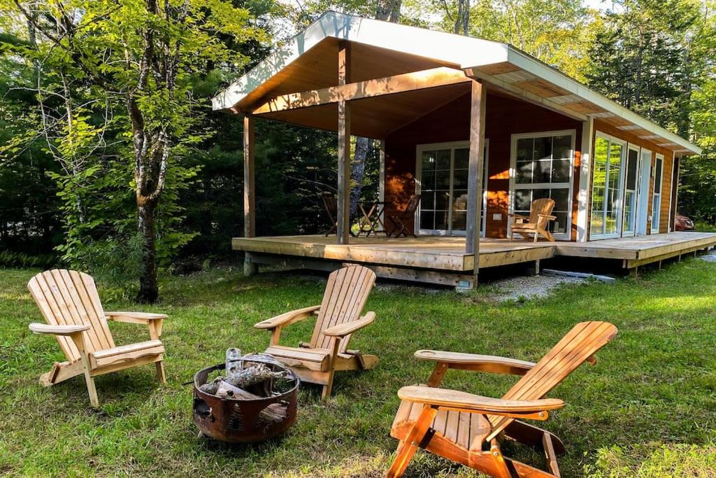 eine Gruppe Stühle und ein Haus im Gras in der Unterkunft Moose Cabin - Cozy Forest Retreat nearby Lake in East Kemptville