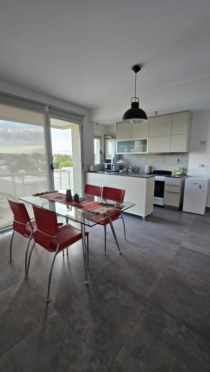 a kitchen with a glass table and red chairs at Departamento Villarino in Puerto Madryn