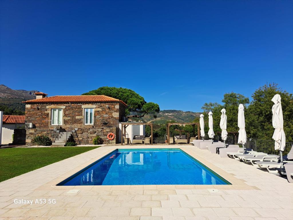 a pool in front of a house with chairs and umbrellas at Quinta da Portelada in Peso da Régua