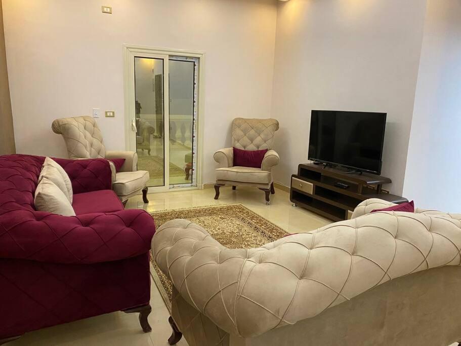 ein Wohnzimmer mit einem Sofa, Stühlen und einem TV in der Unterkunft Furnished Apartment in Cairo, شقة مفروشة بجانب مطار القاهرة in Kairo