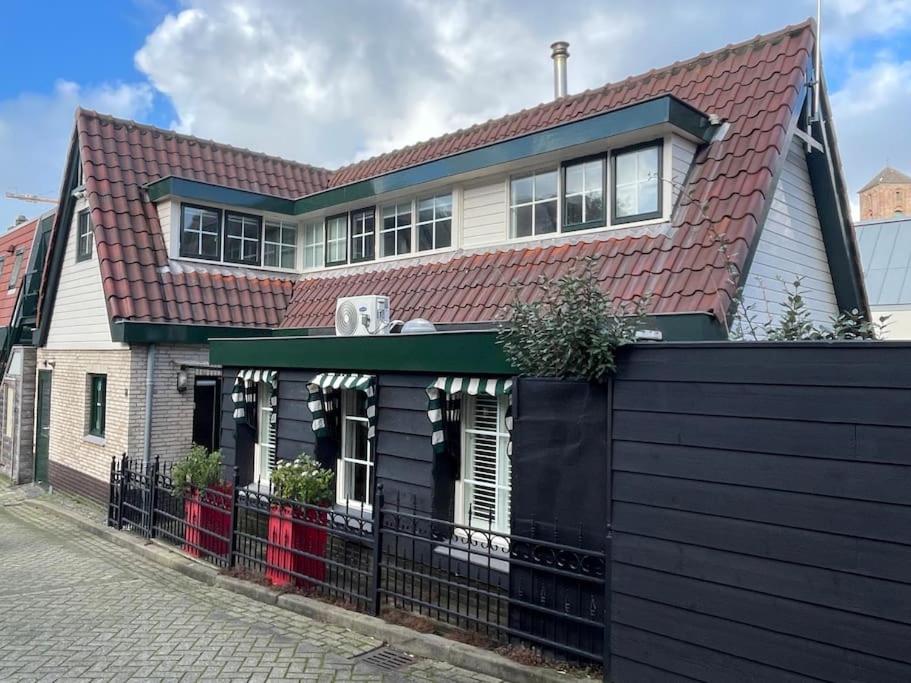 uma casa com um telhado vermelho e uma cerca preta em Fisherman's Cottage - Surf Retreat em Wijk aan Zee