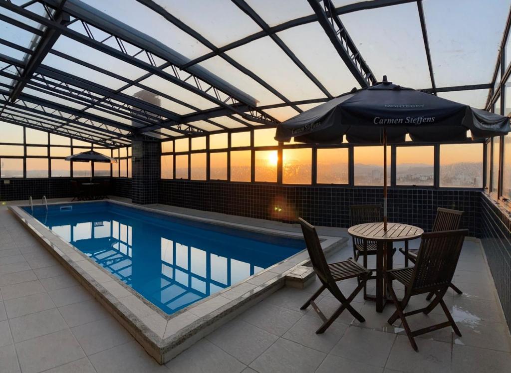 einen Pool mit einem Tisch, Stühlen und einem Sonnenschirm in der Unterkunft Aquarius Hotel Flat Residence in Santa Cruz do Sul
