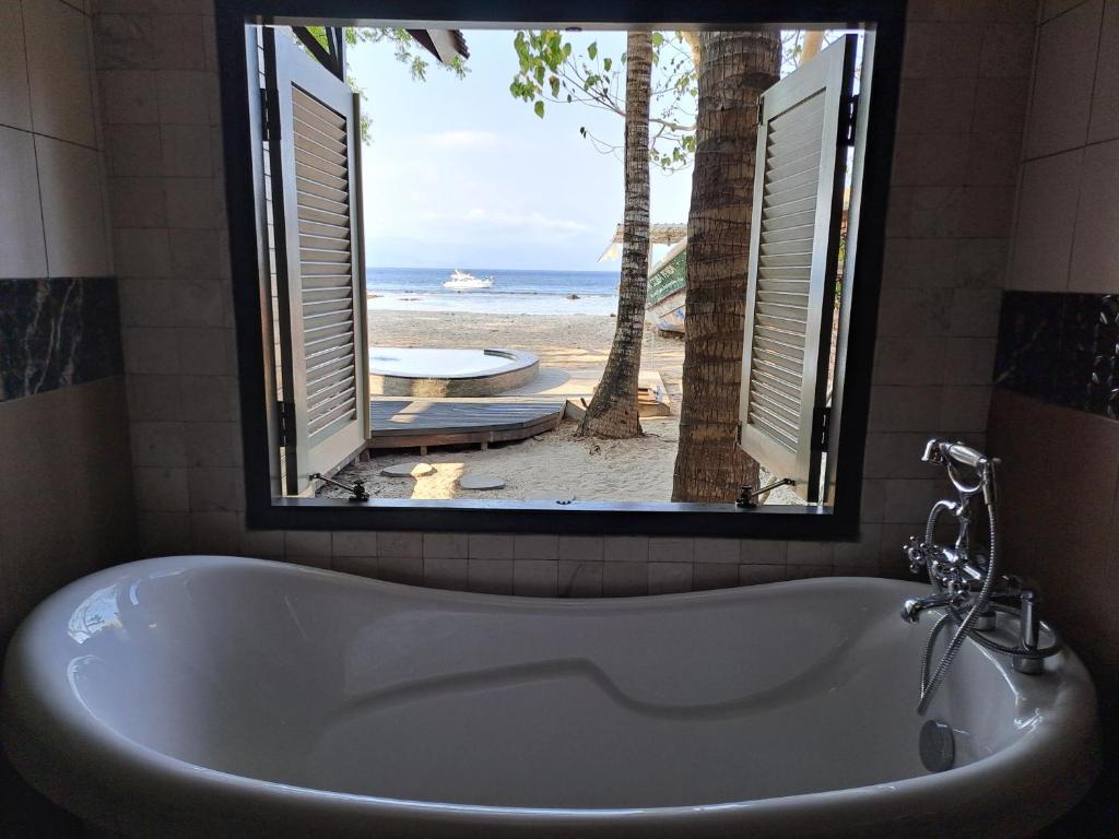 La salle de bains est pourvue d'une baignoire et offre une vue sur la plage. dans l'établissement Beach House Penida, à Nusa Penida