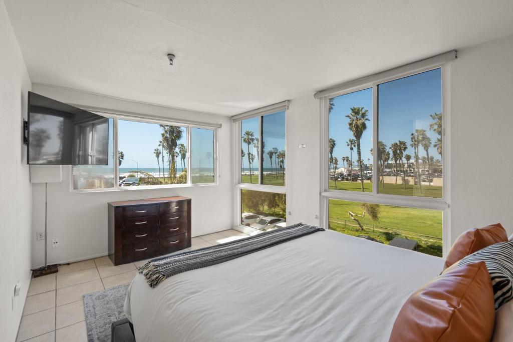 a bedroom with a bed and a tv and windows at Belmont Modern - Ocean View, Pet Friendly, Patio in San Diego