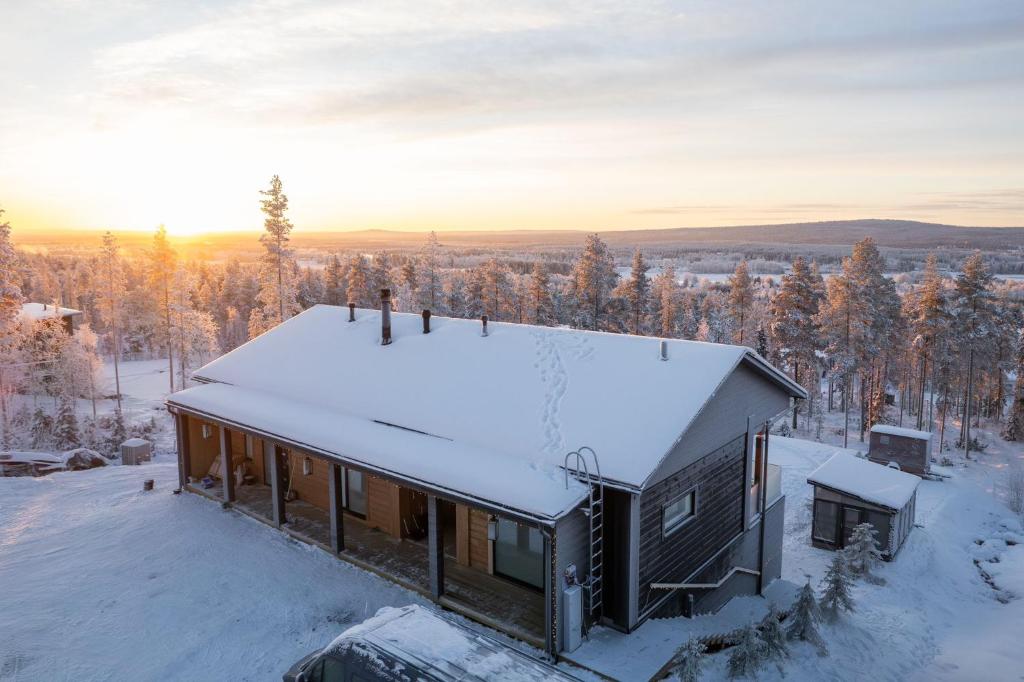 a house covered in snow with the sun setting in the background at Villa Vaalea in Rovaniemi