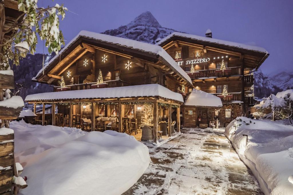 a log cabin in the snow with mountains in the background at Hotel Chalet Svizzero in Courmayeur