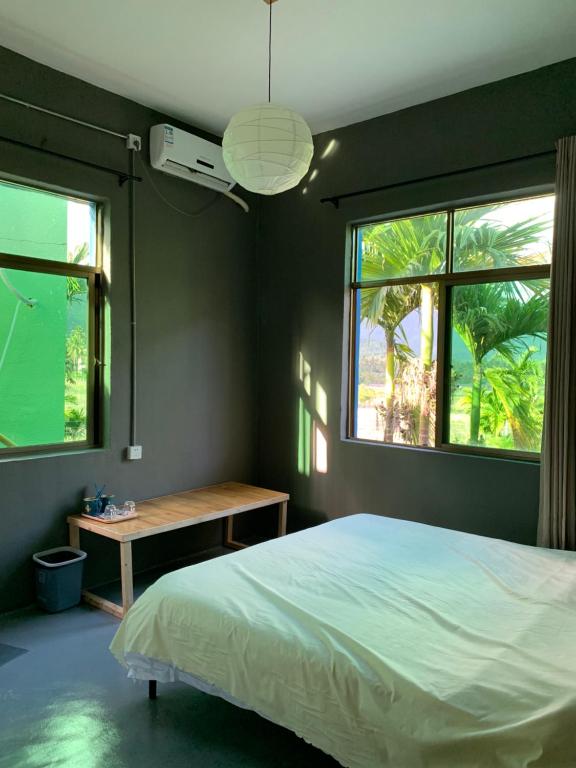 a bedroom with a bed and a table and two windows at GAR'S Homestay in Wanning