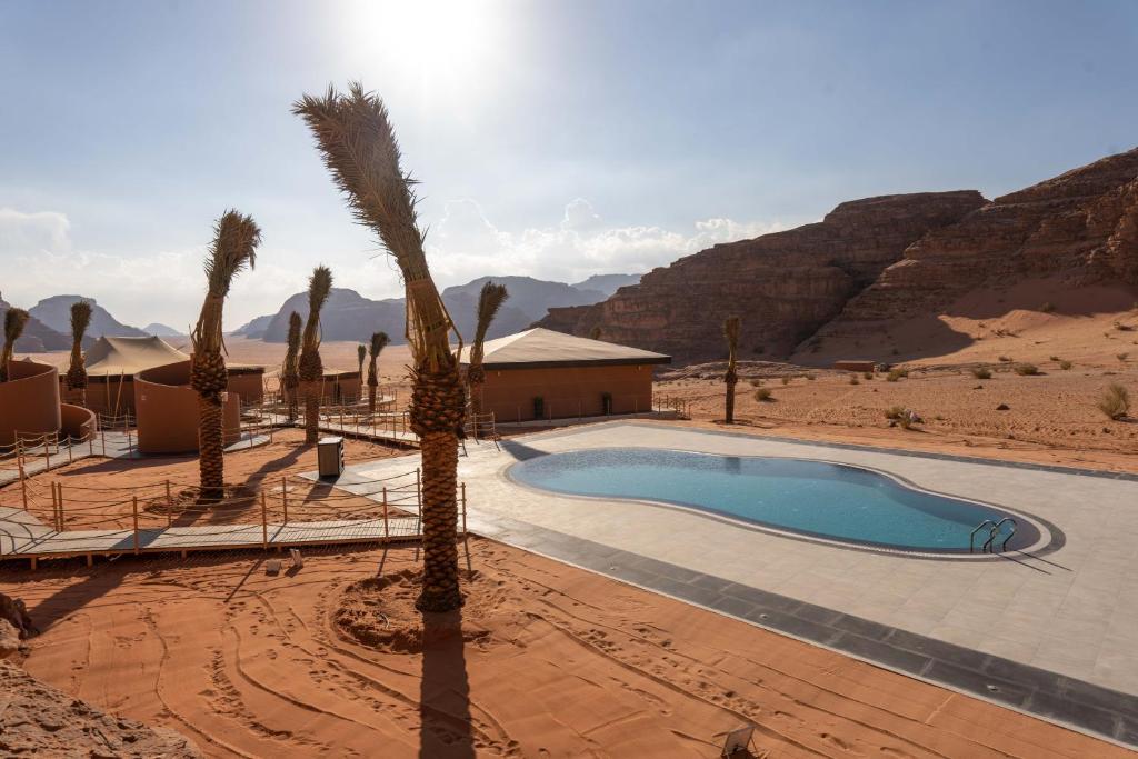 una piscina en el desierto con palmeras y un edificio en Valley Resort en Wadi Rum