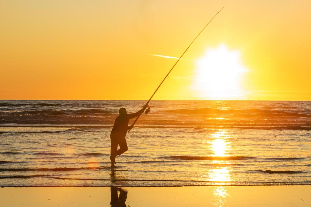 um homem pescando na praia ao pôr do sol em Foxton Beach Holiday Park em Foxton Beach