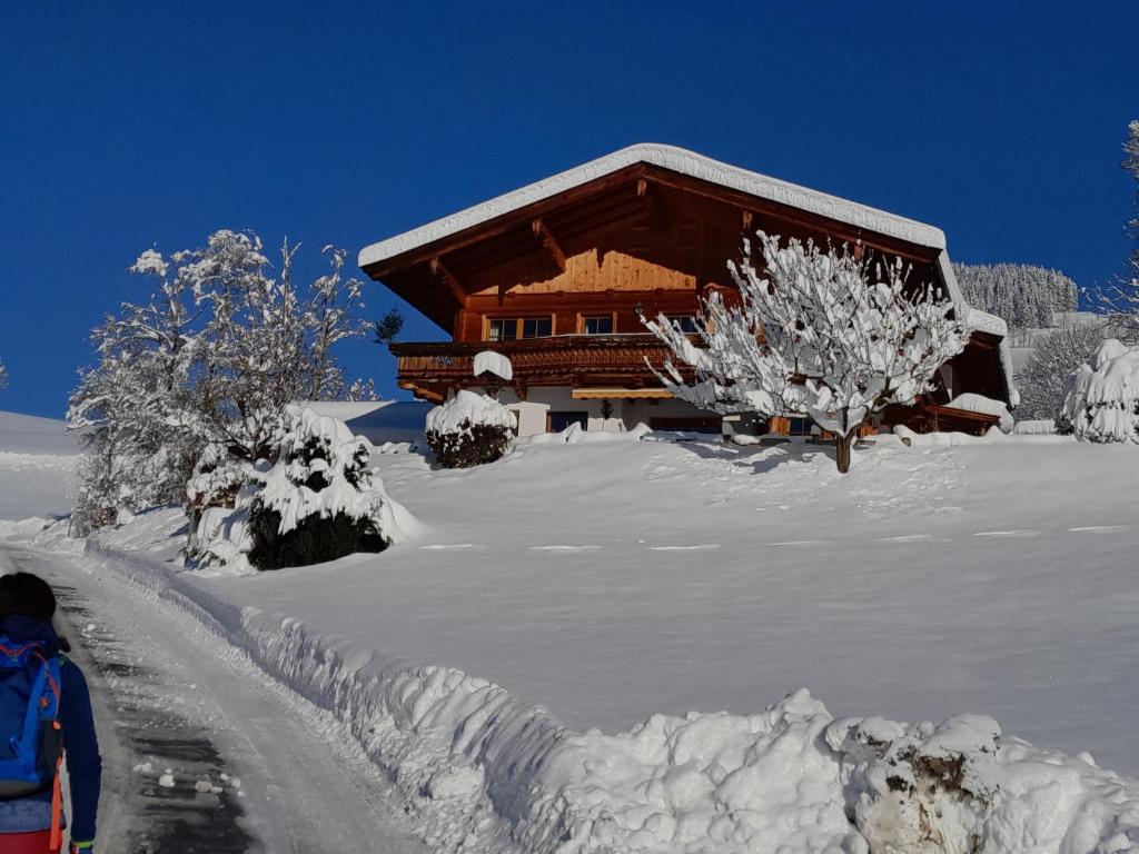 une cabane en rondins recouverte de neige à côté d'une route dans l'établissement Ferienwohnung Obernauer, à Aurach bei Kitzbuhel