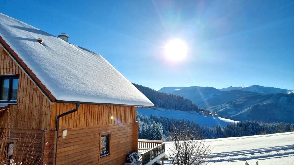 a wooden building with a snow covered roof with mountains in the background at Ferienhaus Lärchenhütte in Kasperle