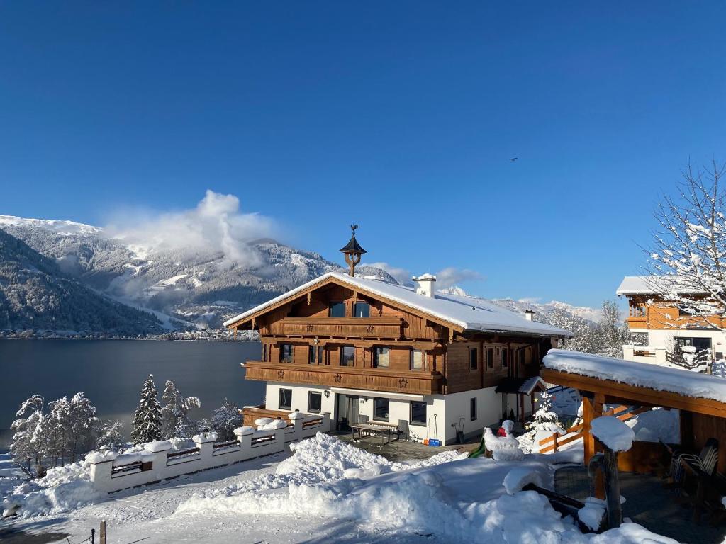 a house in the snow with a lake and mountains at Erlbruckhof in Zell am See