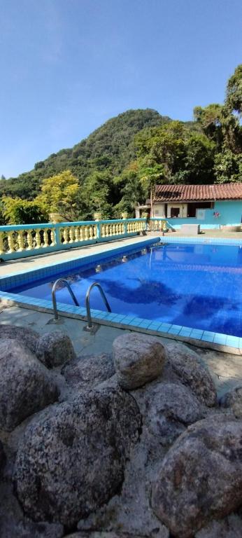 a blue swimming pool with rocks in front of a house at Chalé Mirante do Félix (Amarelo) in Ubatuba
