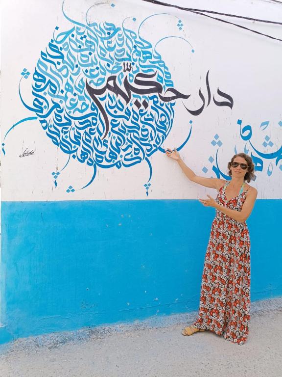 a woman standing in front of a wall with a painting at Dar Hkaïem in Sousse