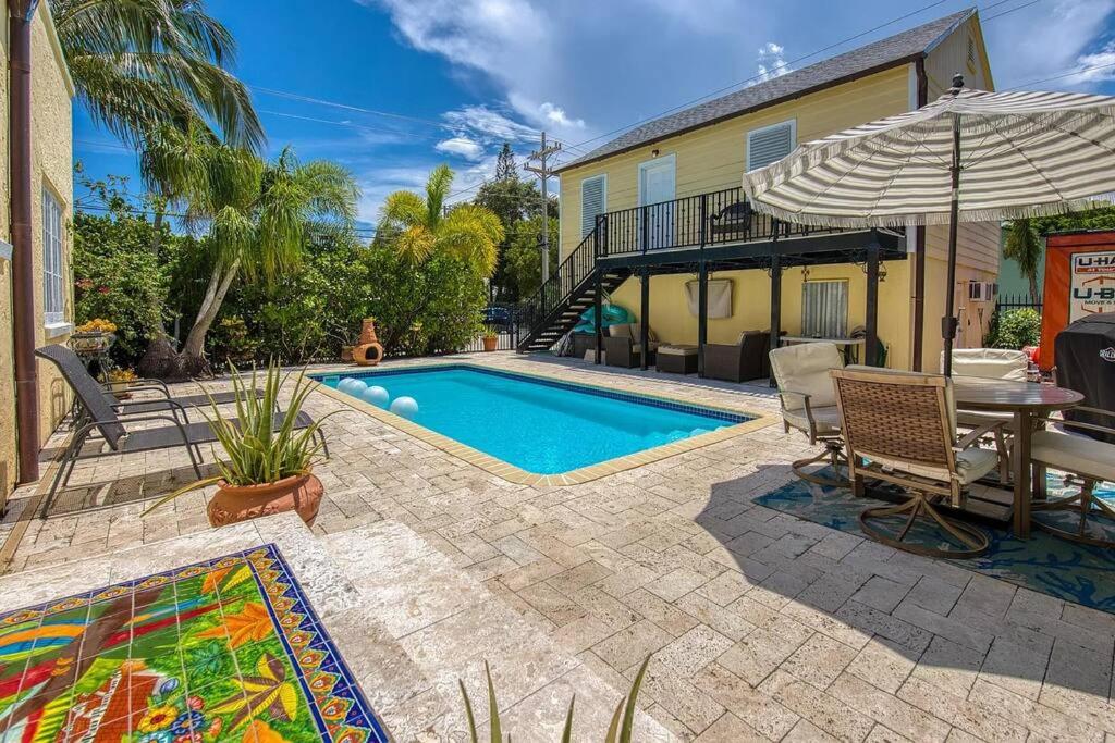 un patio trasero con piscina, mesa y sombrilla en Charming Villa Espagna - Heated/Salt-Pool Oasis!, en Lake Worth