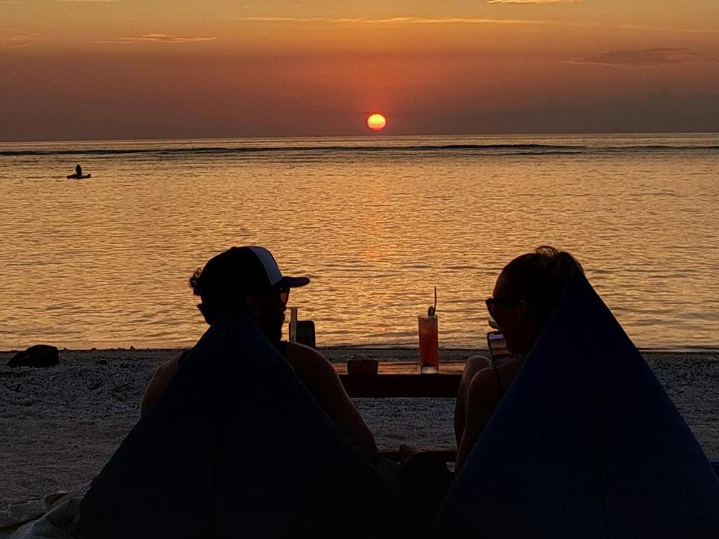 dos personas sentadas en la playa viendo la puesta de sol en Salabose Cottages, en Gili Air