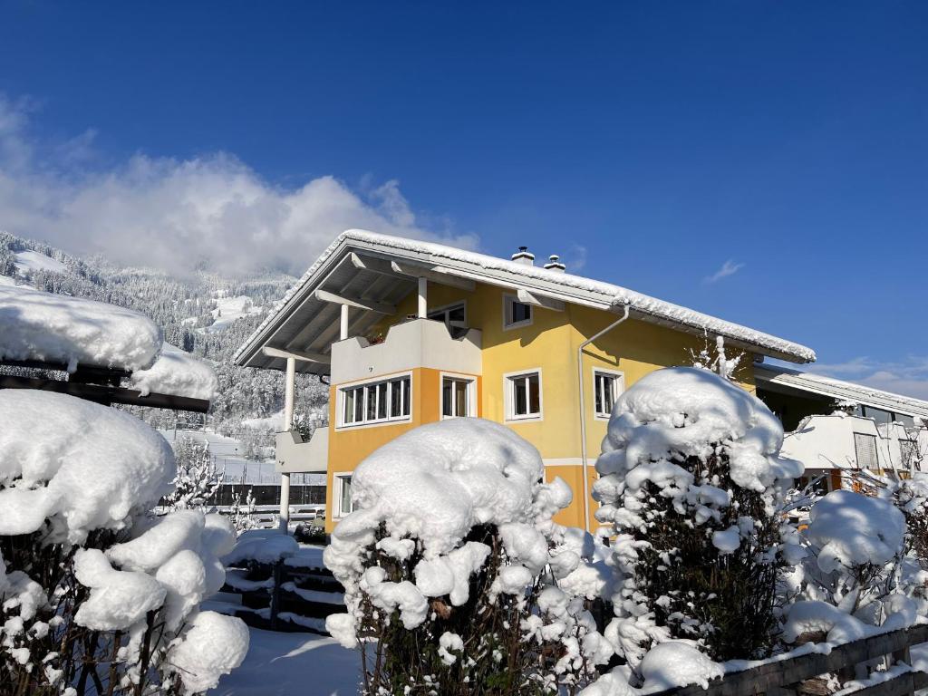 a yellow house covered in snow with snow covered trees at Appartement Christine in Sankt Johann im Pongau