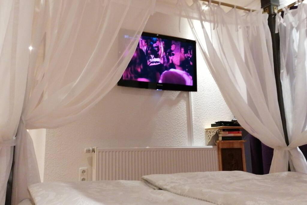 1 dormitorio con cortinas blancas y TV en la pared en Romantisches Cottage - besonderer Rückzugsort auf Hofreite von 1784, en Gründau