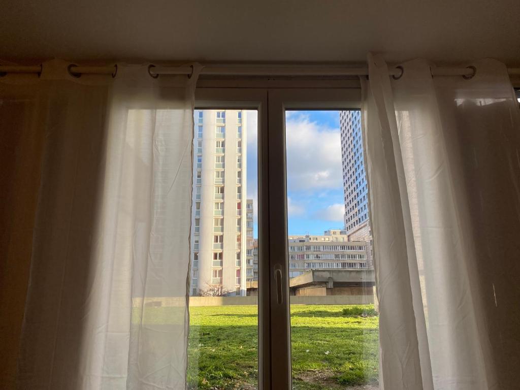 a window with white curtains with a view of a building at Luxsuite in Aubervilliers