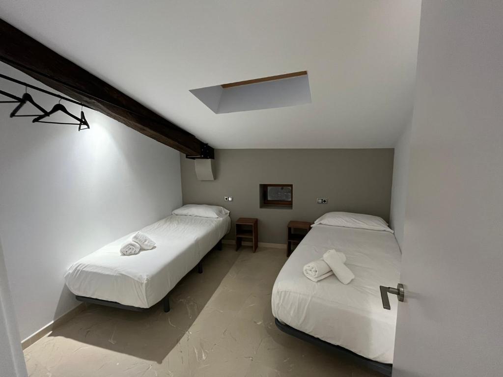2 camas en una habitación pequeña con sábanas blancas en Antiga Biblioteca en Solsona
