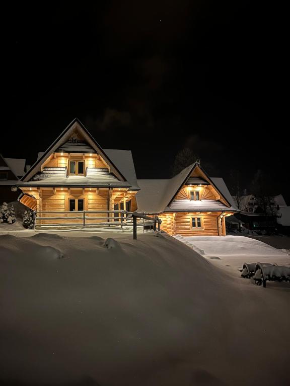 ein Haus mit nachts eingeschalteten Lichtern im Schnee in der Unterkunft Domki WIDOKÓWKA in Bukowina Tatrzańska