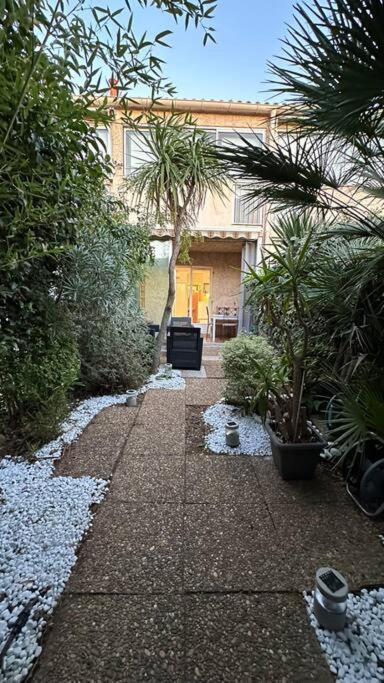 un jardin avec une passerelle ornée de plantes et un bâtiment dans l'établissement Studio coin nuit fermé 4 personnes - Les Mas de La Plage, à Sanary-sur-Mer