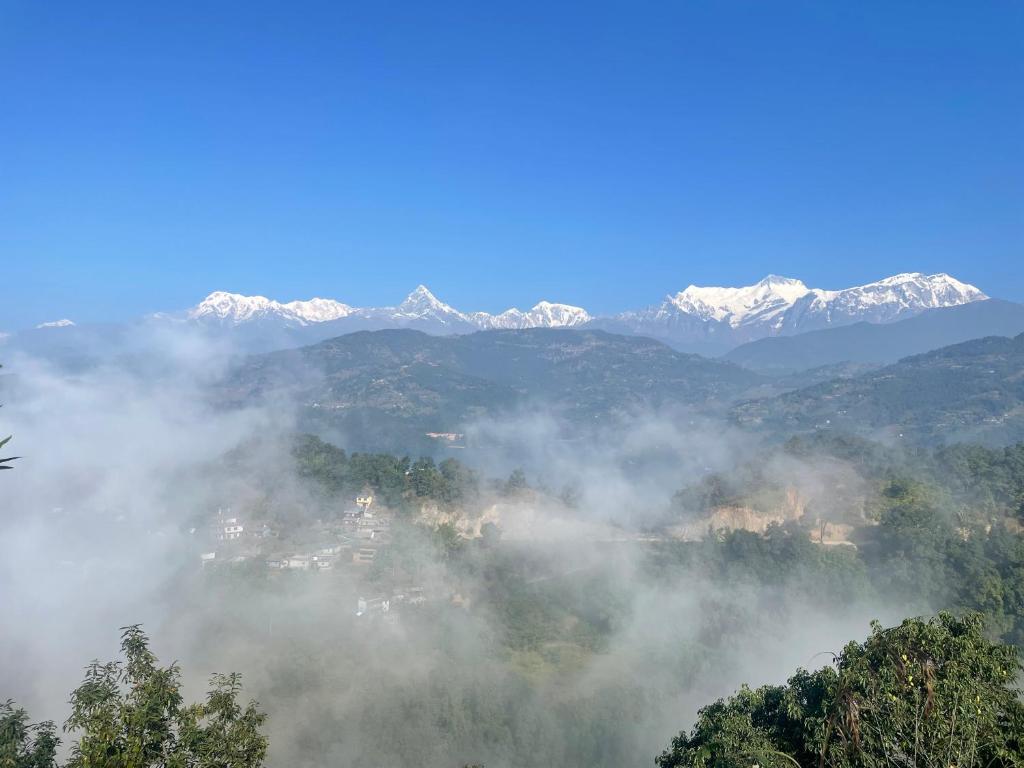 un valle nebuloso con montañas cubiertas de nieve en el fondo en Himalaya Serene View Guest House & Farm Stay en Deorāli