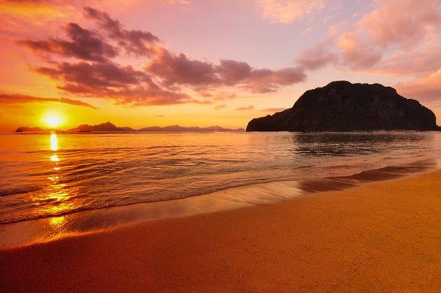 una puesta de sol en una playa con una roca en el agua en Calitang Pearl Cottage en Nacpan