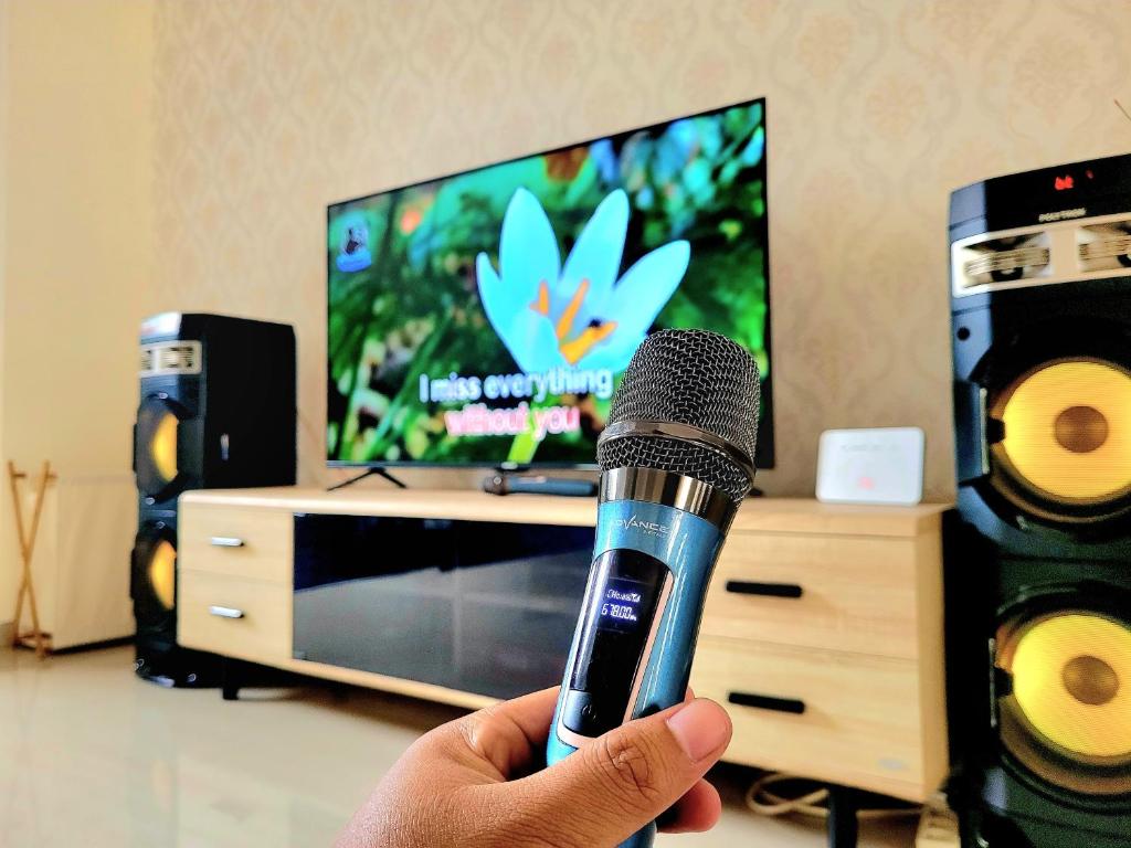 una persona sosteniendo un micrófono frente a una televisión en MG'S Villa en Batu