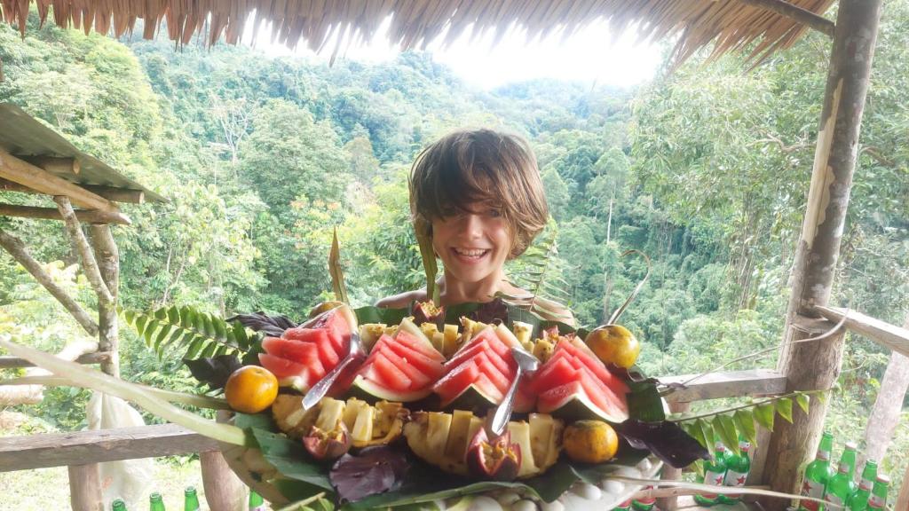 a person holding a plate of fruit in front of a forest at LOVELY JUNGLE LODGE & JUNGLE TREKING only book with us in Bukit Lawang